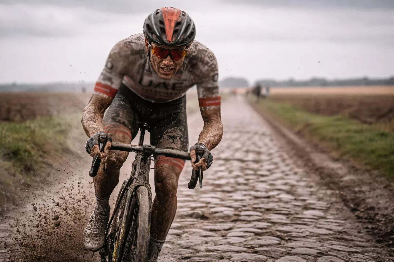 Ciclista cubierto de barro pedaleando sobre los adoquines de la París-Roubaix
